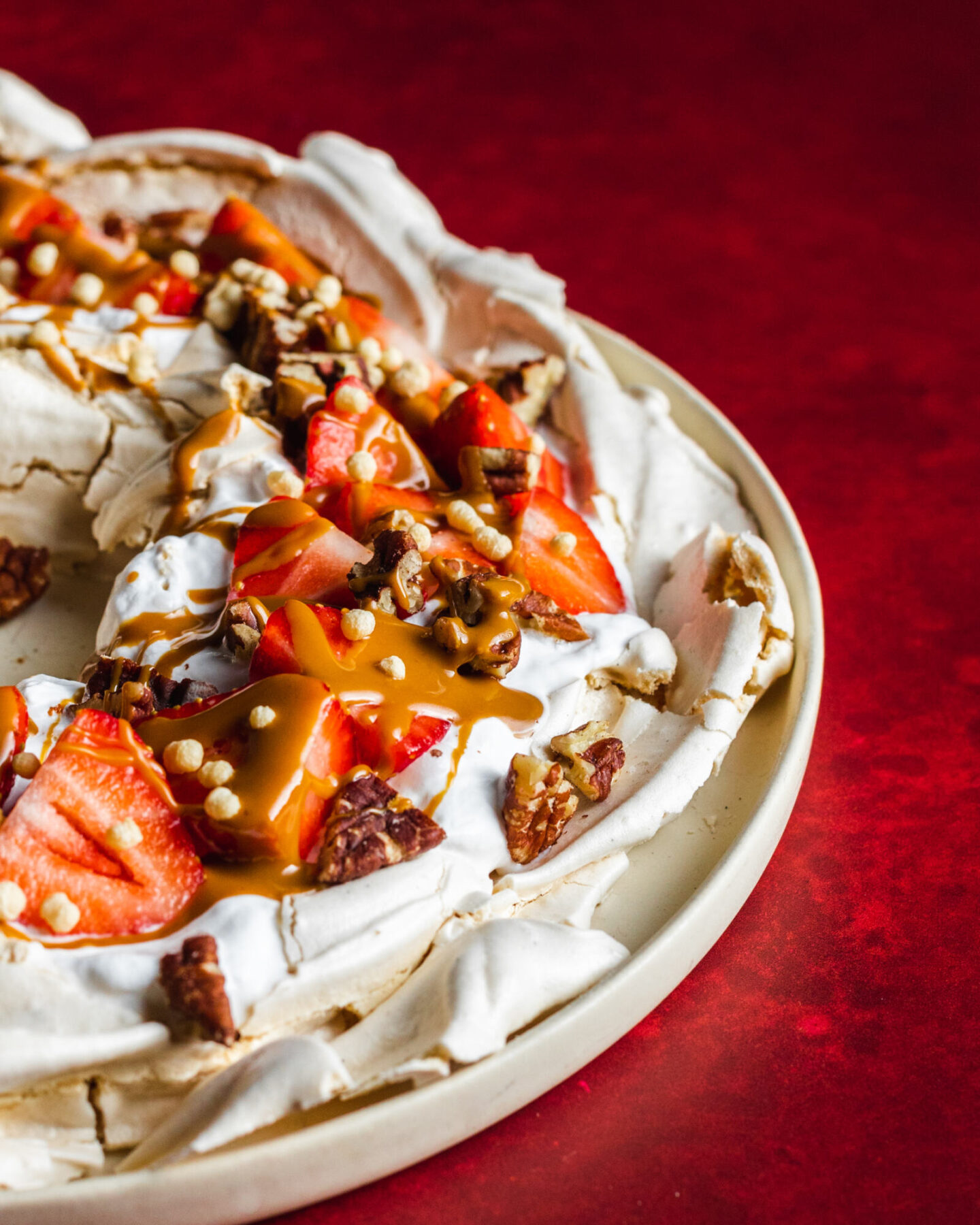 Vegan Meringue wreath, photographed from the side with the crunchy pavlova edge visible, topped with vegan whipped cream, strawberries and nuts