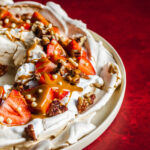 Vegan pavlova wreath made with aqauafaba meringue, topped with strawberries, whipped coconut cream and toasted pecan nuts