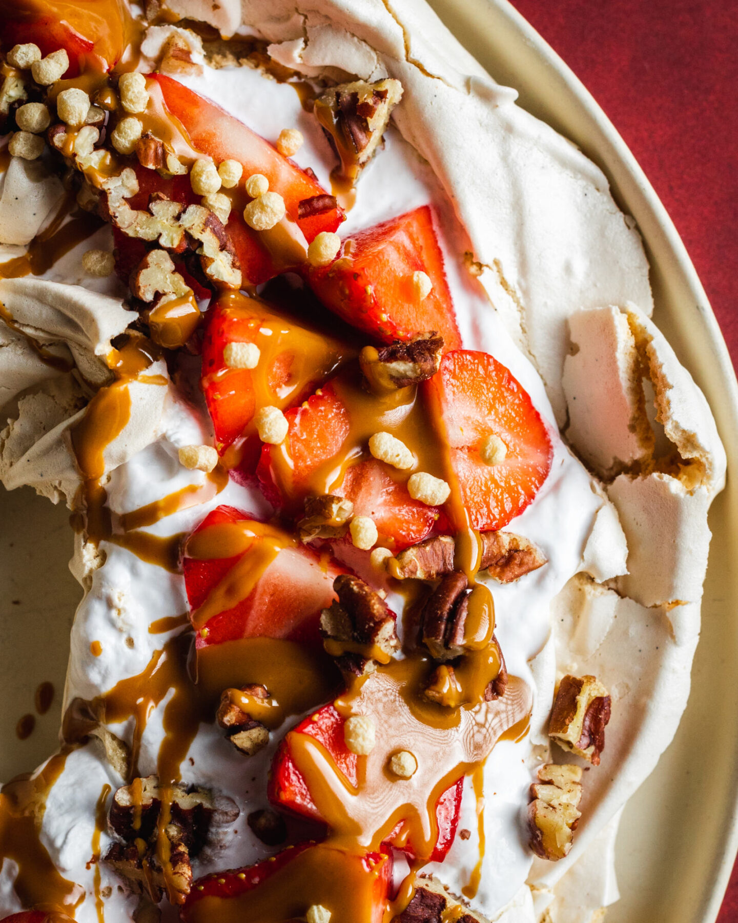 Vegan pavlova photographed from the top, with whipped coconut cream, strawberries, nuts and peanut butter on top 