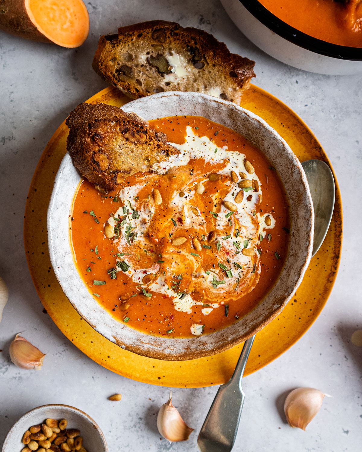 a bowl full of red pepper and sweet potato soup with a slice of toasted bread on the siide