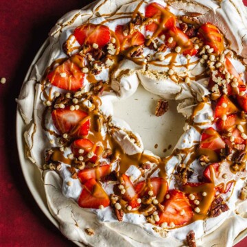 Vegan pavlova wreath made with aqauafaba meringue, topped with strawberries, whipped coconut cream and toasted pecan nuts