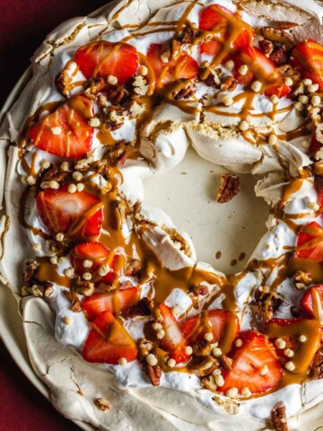 Vegan pavlova wreath made with aqauafaba meringue, topped with strawberries, whipped coconut cream and toasted pecan nuts