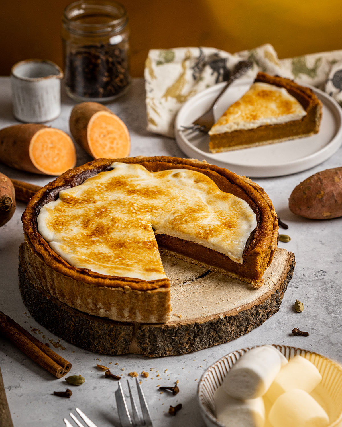 A whole sweet potato pie with one slice cut out of it surrounded by ingredients such as sweet potato vegan marshmallows and spices.
