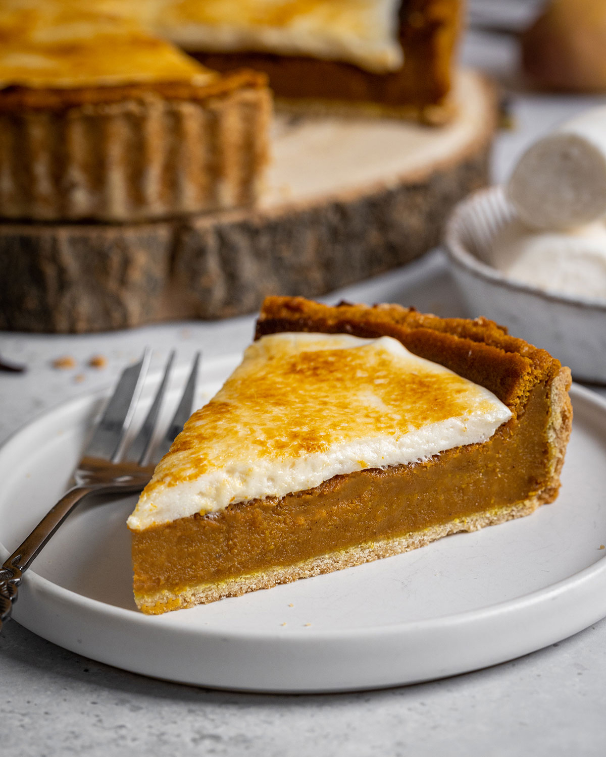 A slice of vegan sweet potato pie on a white plate alongside a desert fork, with the entire sweet potato pie in the background.