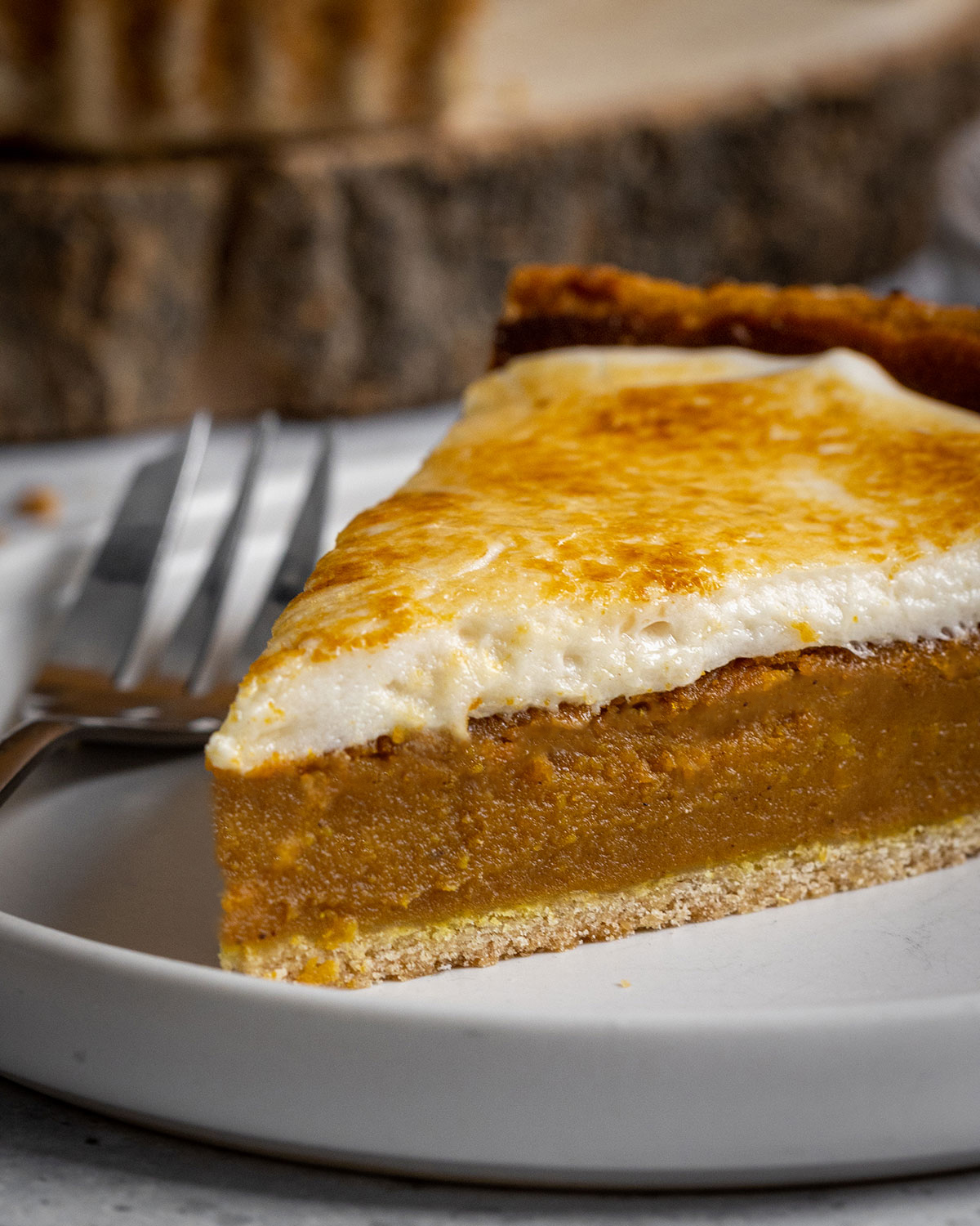 A close-up photograph of a vegan sweet potato pie slice, with the creamy sweet potato filling, the home-made vegan pie crust, and smooth marshmallow frosting clearly visible.