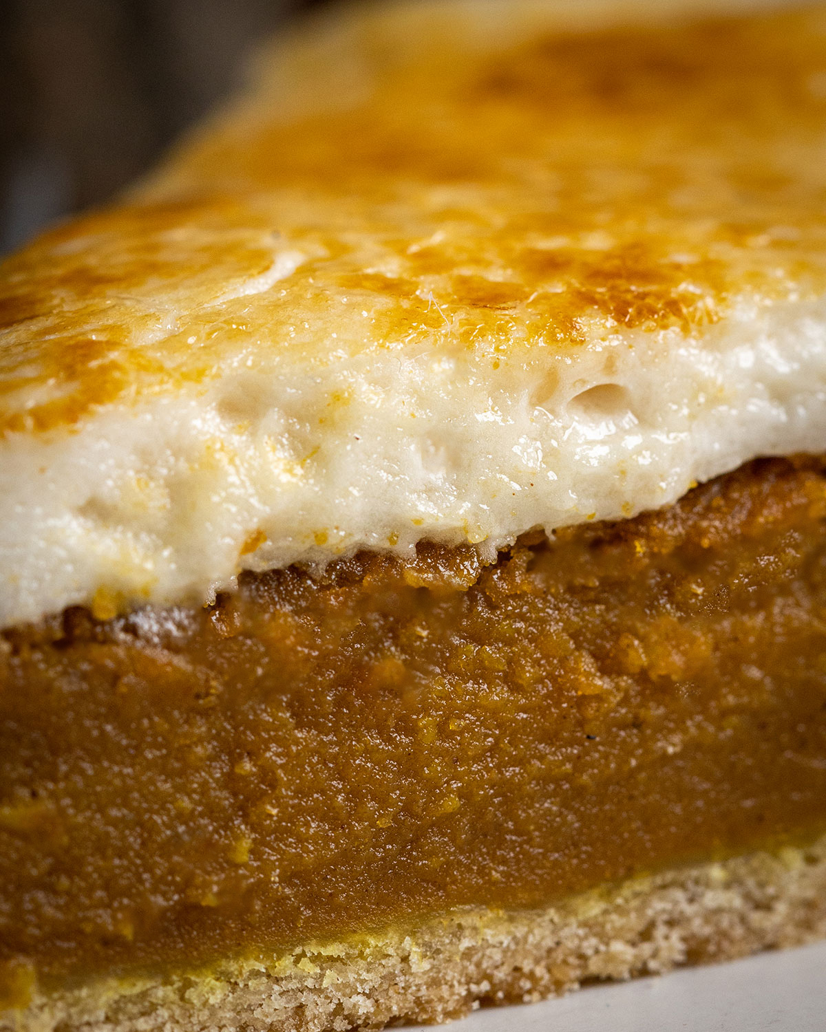 Extremely close up photograph of a vegan sweet potato pie slice, with the layers of home-made pie crust, most sweet potato pie filling and soft vegan marshmallow frosting clearly visible.