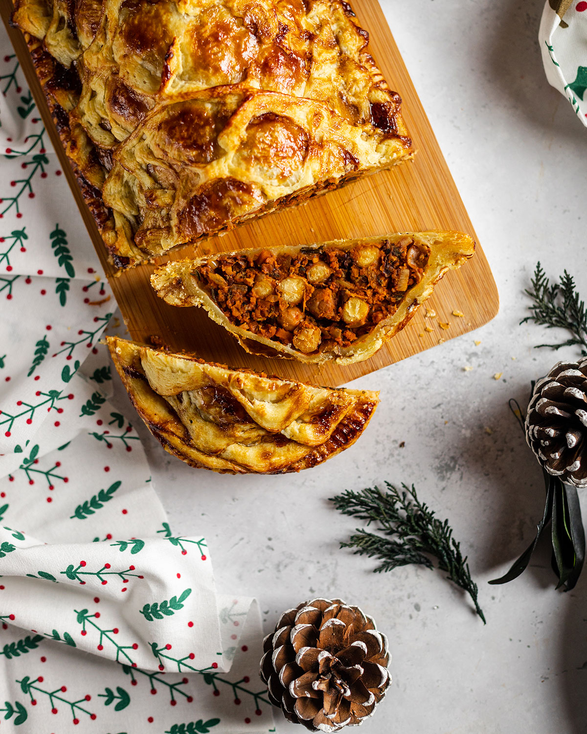 A slice vegan Wellington on a chopping board sitting on a marbled white table surrounded by Christmas decoration