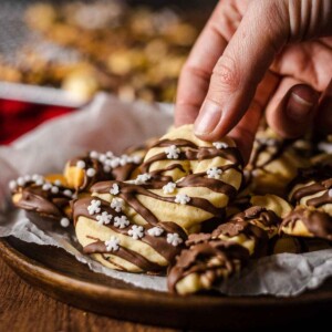 a hand picking up a vegan spritz cookie from a plate filled with cookies