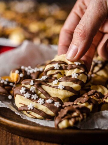 a hand picking up a vegan spritz cookie from a plate filled with cookies