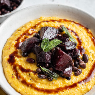 A serving bowl is filled with creamy pumpkin polenta and topped with roasted beetroot.