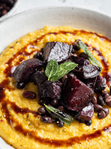 A serving bowl is filled with creamy pumpkin polenta and topped with roasted beetroot.