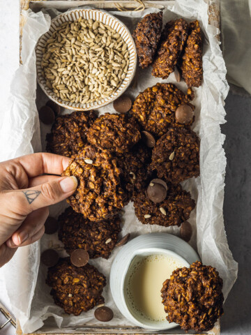 A box is filled with sunflower seed cookies and a hand is coming in from the left to pick up a cookie.