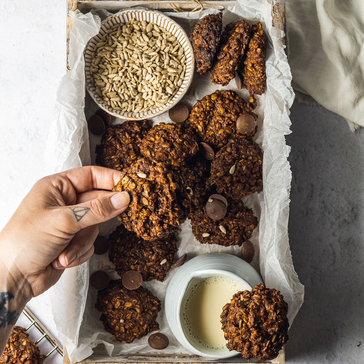 A box is filled with sunflower seed cookies and a hand is coming in from the left to pick up a cookie.