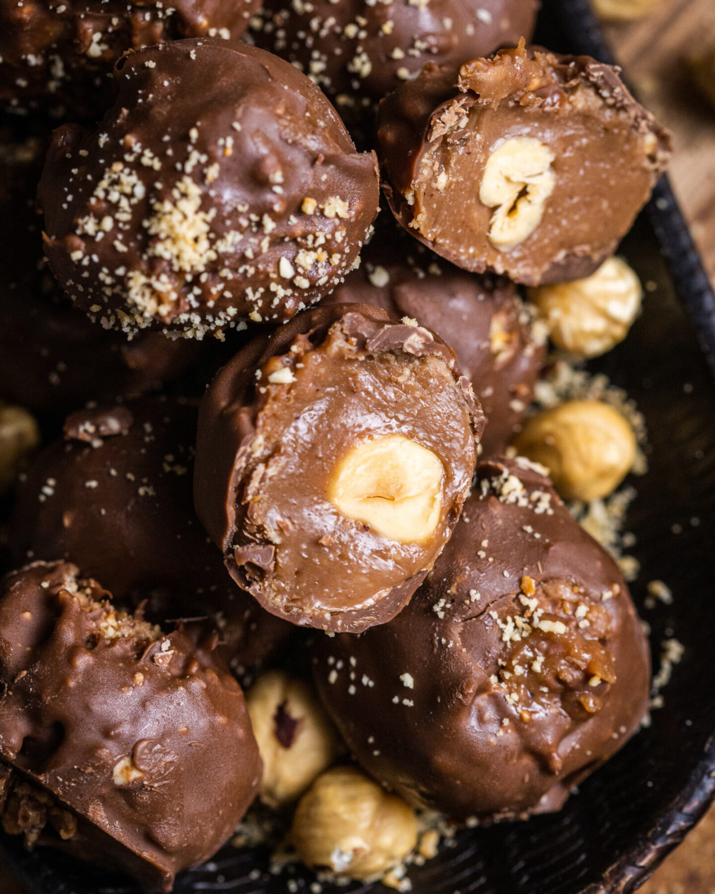 A vegan chocolate hazelnut truffle cut in half with the smooth and creamy chocolate hazelnut filling visible alongside the blanched hazelnuts in the middle