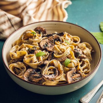 A round bowl is filled with vegan mushroom pasta and served with fresh sage leaves.