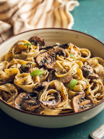 A round bowl is filled with vegan mushroom pasta and served with fresh sage leaves.