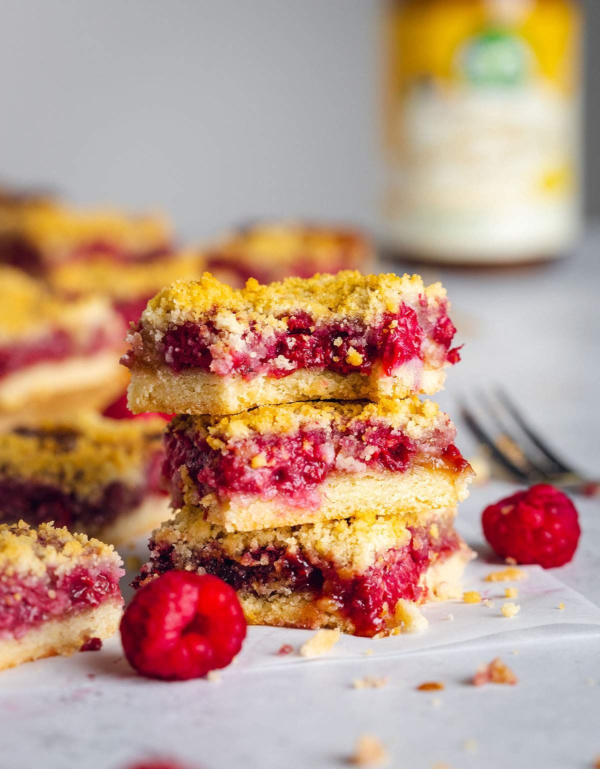 Three butterscotch bars are stacked with a bite taken out of the one on top. The scene is surrounded by more bars on a white table and you can distinguish a yellow jar and a fork in the background.