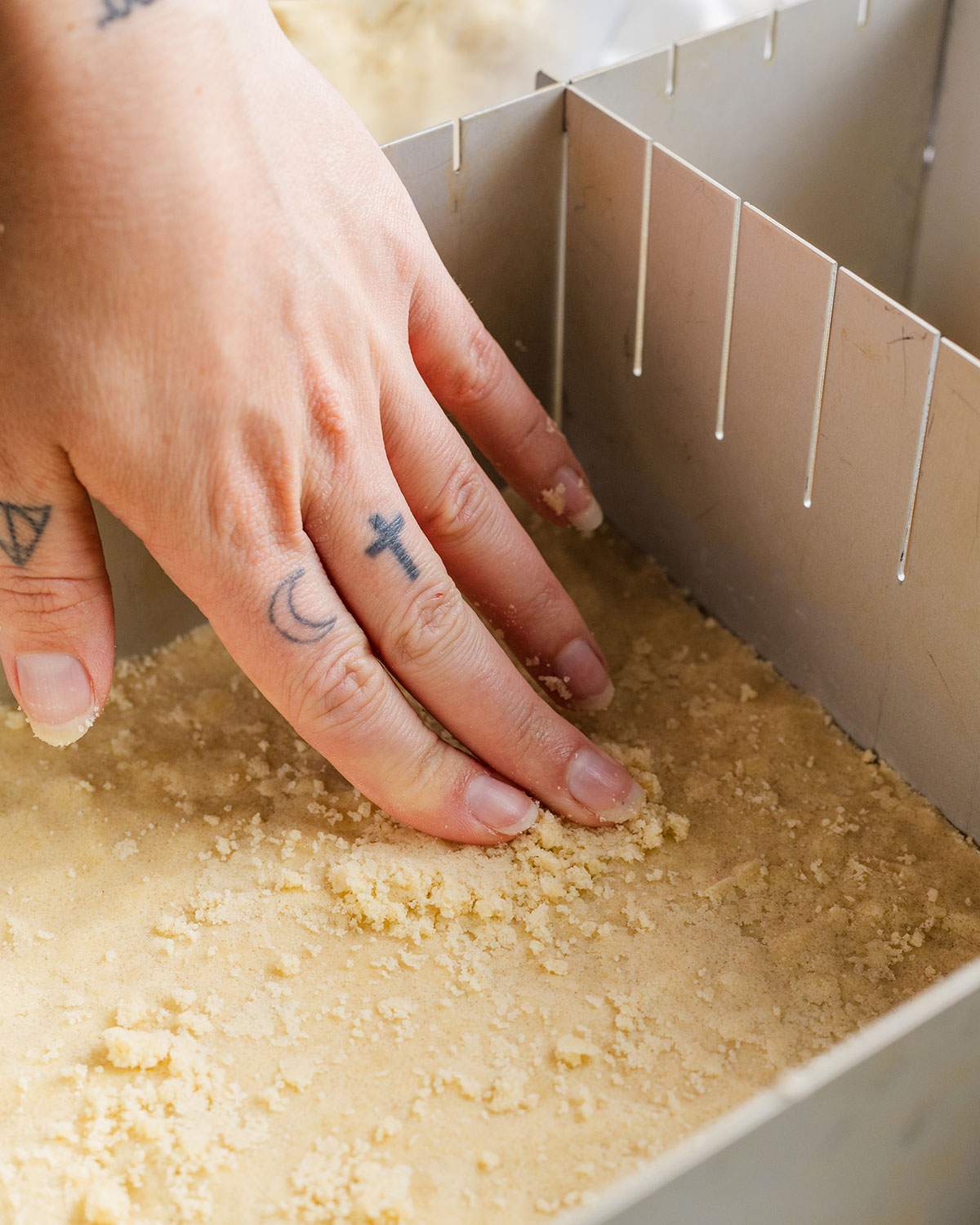 A hand is pressing part of the crumble mix into the bottom of the oven dish to create the base.