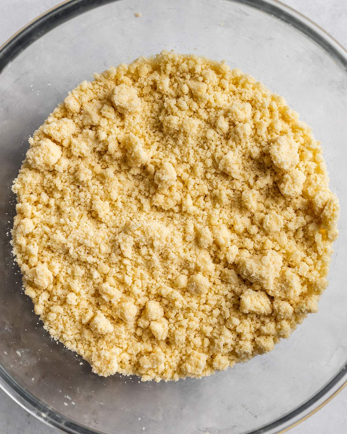 The crumble mix is shown in a glass bowl and its texture is coarse and crumbly.