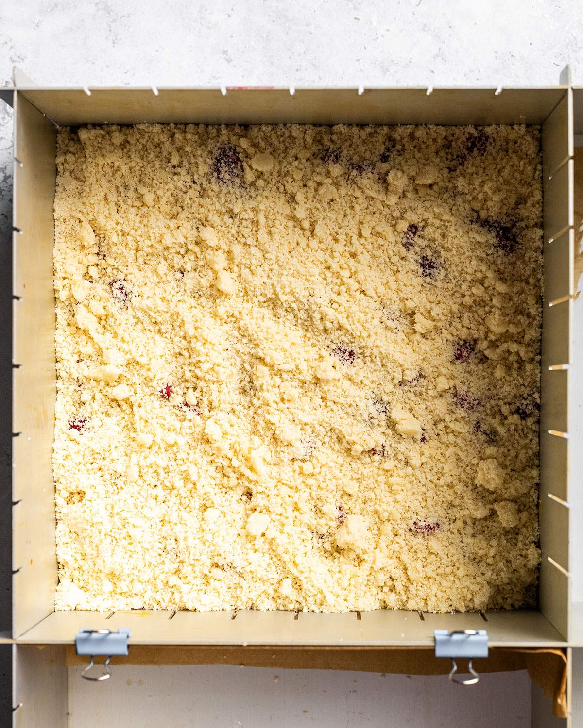 A square size Butterscotch raspberry crumble is shown in a baking dish before baking.