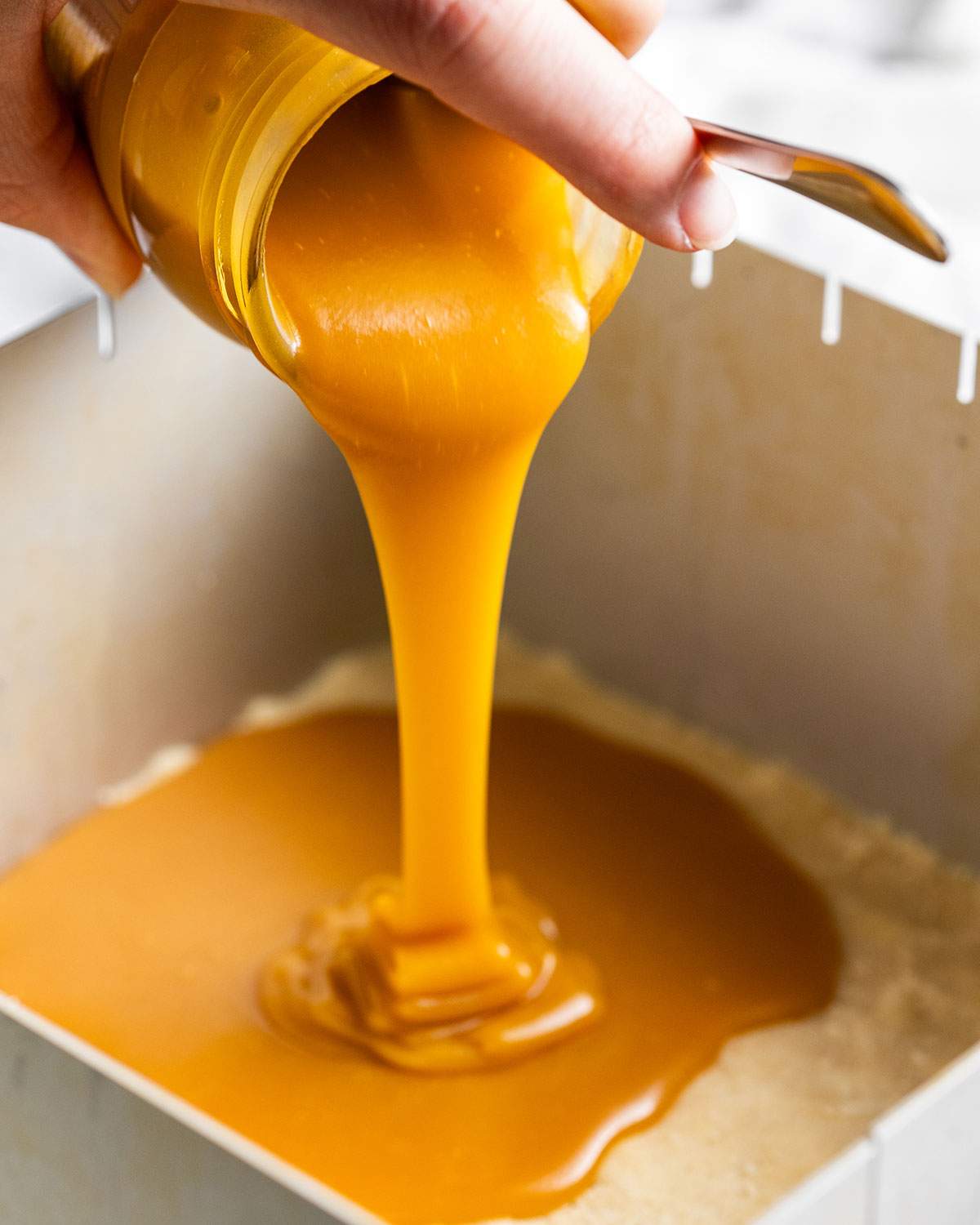 A hand is pouring a jar of vegan butterscotch sauce into the baking dish straight from the jar.