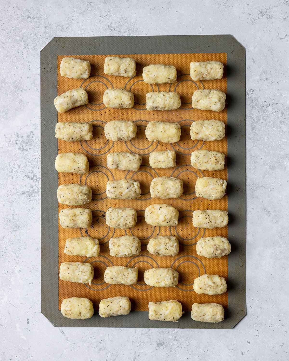 Potato tots neatly arranged on silicone baking mat