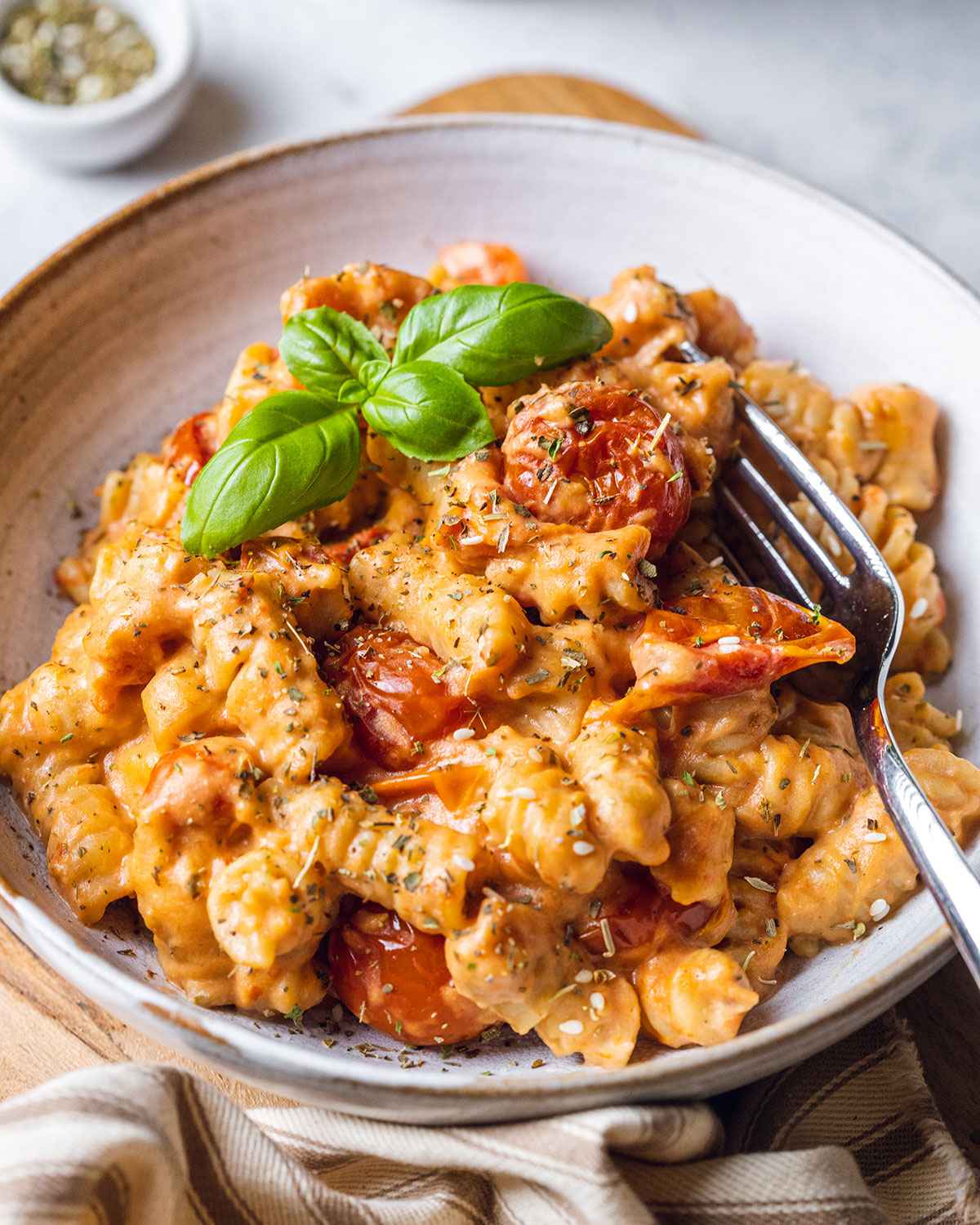 creamy baked boursin pasta in a white bowl, topped with fresh basil