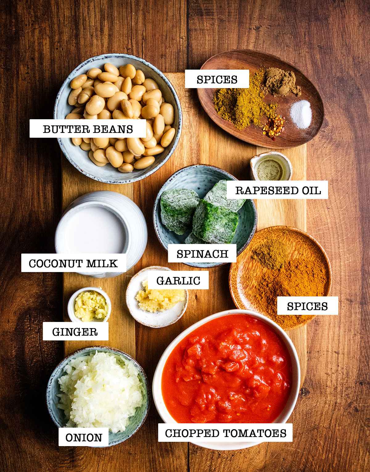 All ingredients for butter bean curry are pre-measured on a wooden board on the table and each ingredient is labelled.