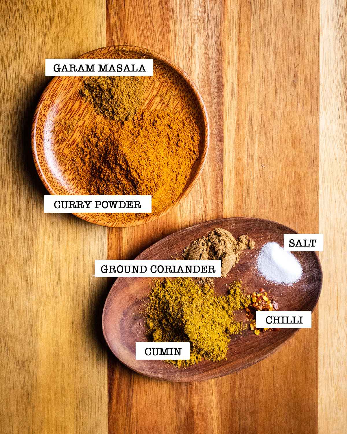 All the spices and seasoning used in the curry are shown on two small wooden dishes with a label next to each ingredient.