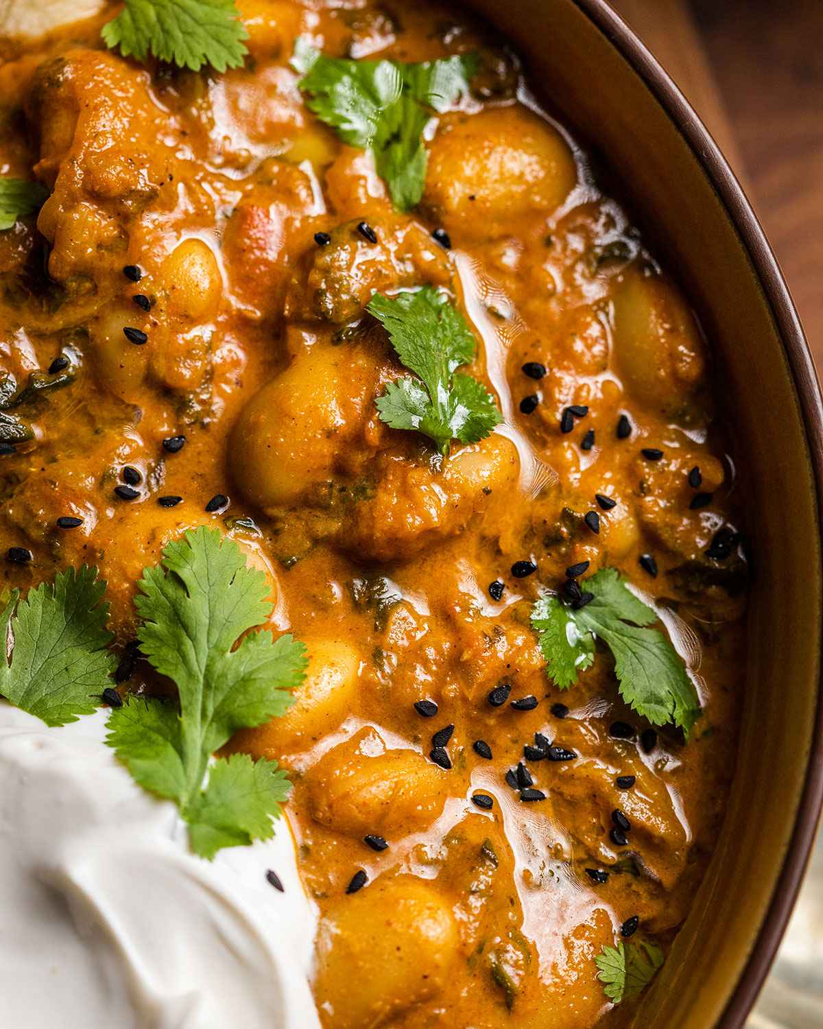creamy vegan butter bean curry in a bowl with fresh herbs on top and coconut yogurt on the side