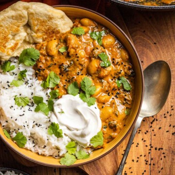 delicious vegan butter bean curry recipe in a yellow bowl alongside homemade naan bread, basmati rice, coconut yogurt and fresh coriander