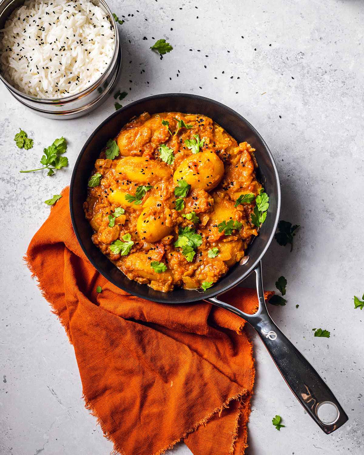 an Olav pan on a white marble table with an orange napkin and vibrant dum aloo recipe in the pan