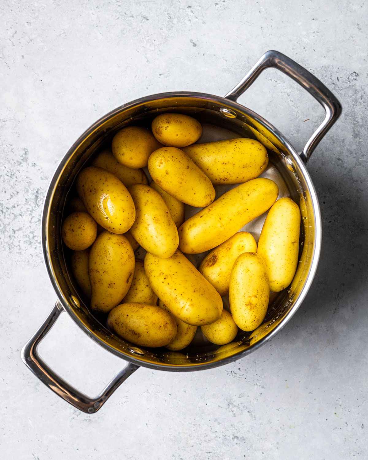 unpeeled potatoes covered in water in a saucepan