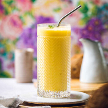 a glass filled with pineapple mango smoothie in front of a colorful background