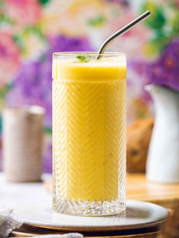 a glass filled with pineapple mango smoothie in front of a colorful background