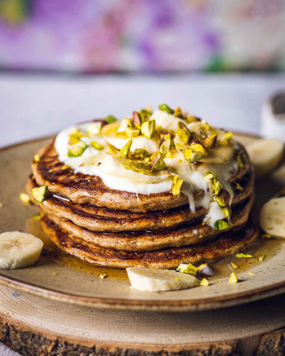 vegan banana pancakes on a beige plate topped with dairy free yogurt, banana slices and pistachio nuts