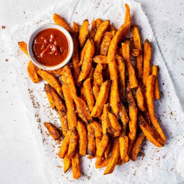 Crispy sweet potato fries on a white sheet with tomato ketchup on the side