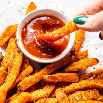 a hand dipping sweet potato fries into a small bowl of tomato ketchup