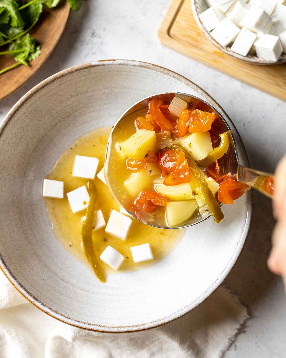 a ladle filled with soup added to the bowl on top of the cheese cubes