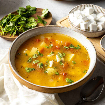 mexican inspired caldo de queso soup in a bowl on the dinner table surrounded by ingredients, such as cheese and fresh cilantro
