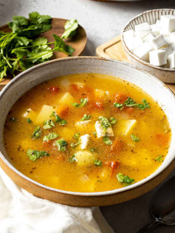 mexican inspired caldo de queso soup in a bowl on the dinner table surrounded by ingredients, such as cheese and fresh cilantro