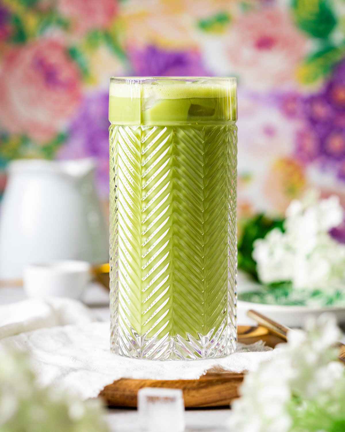 a tall glass with iced matcha surrounded by flowers