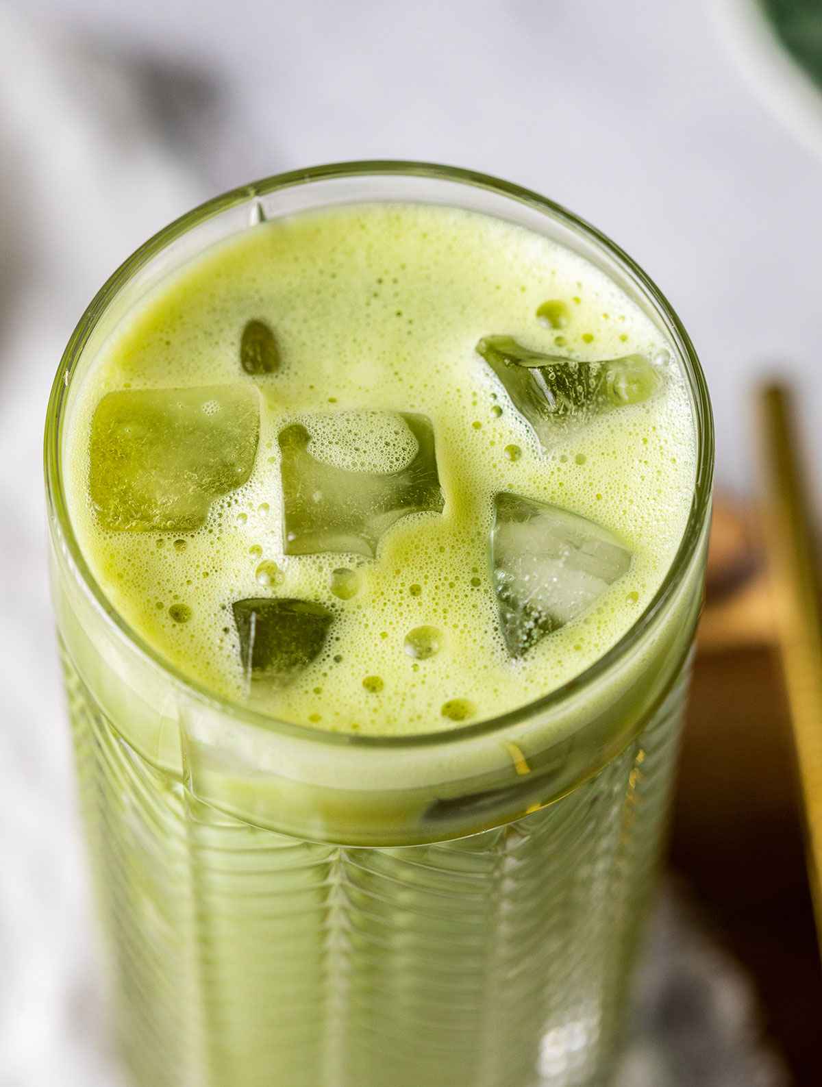 a tall glass filed with iced matcha latte, closely showing the top of the drink and the ice cubes in the glass