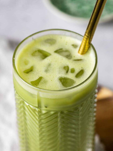 iced matcha latte starbucks style in a tall glass with ice cubes an a metal straw