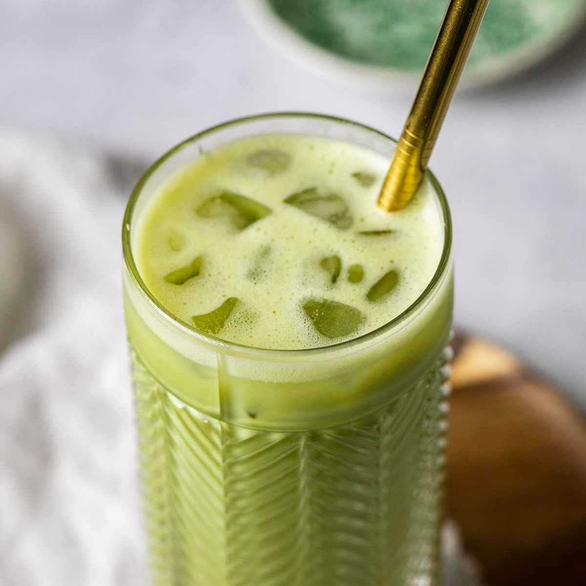 iced matcha latte starbucks style in a tall glass with ice cubes an a metal straw