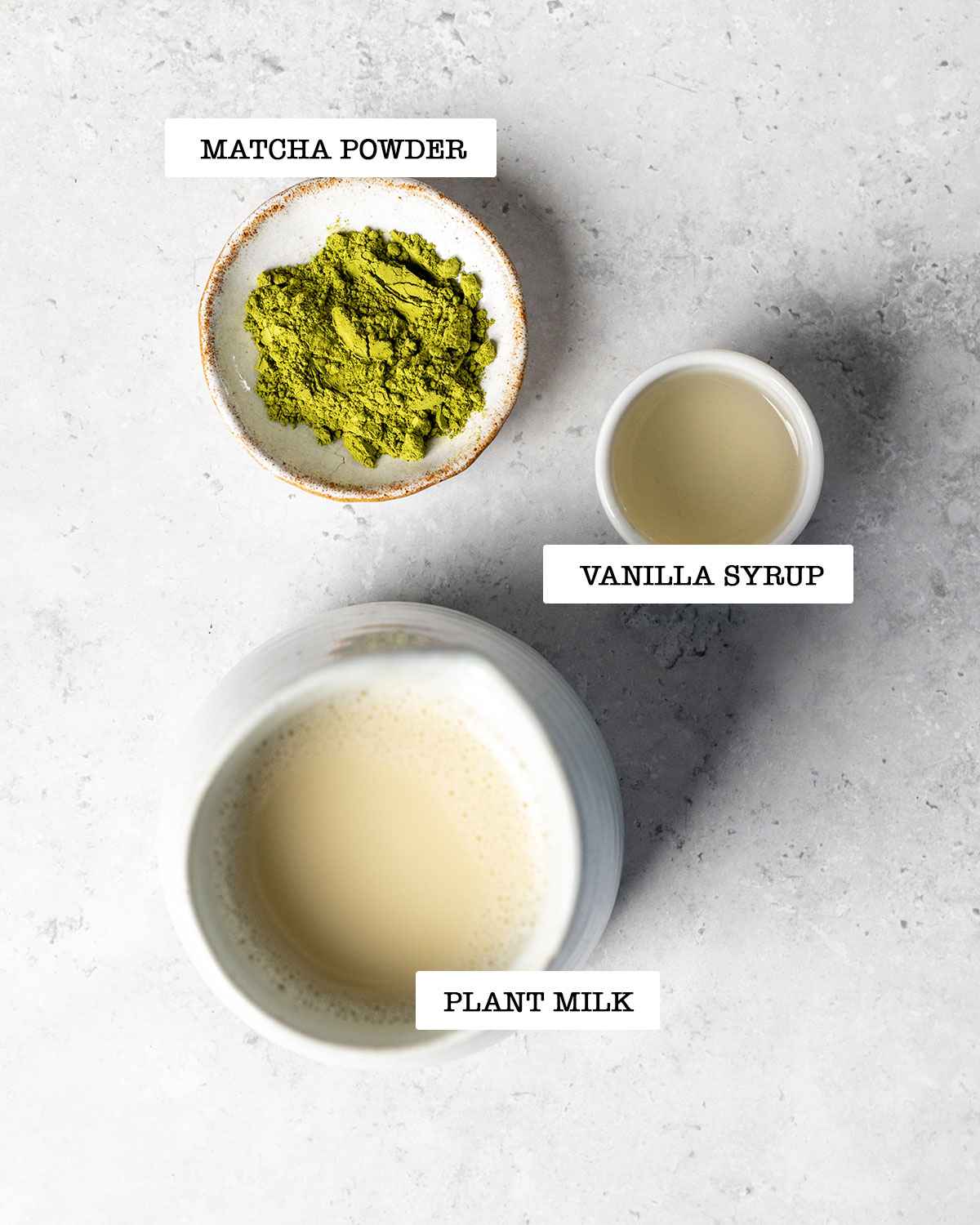 Ingredients for making starbucks matcha latte on a white marble table with labels