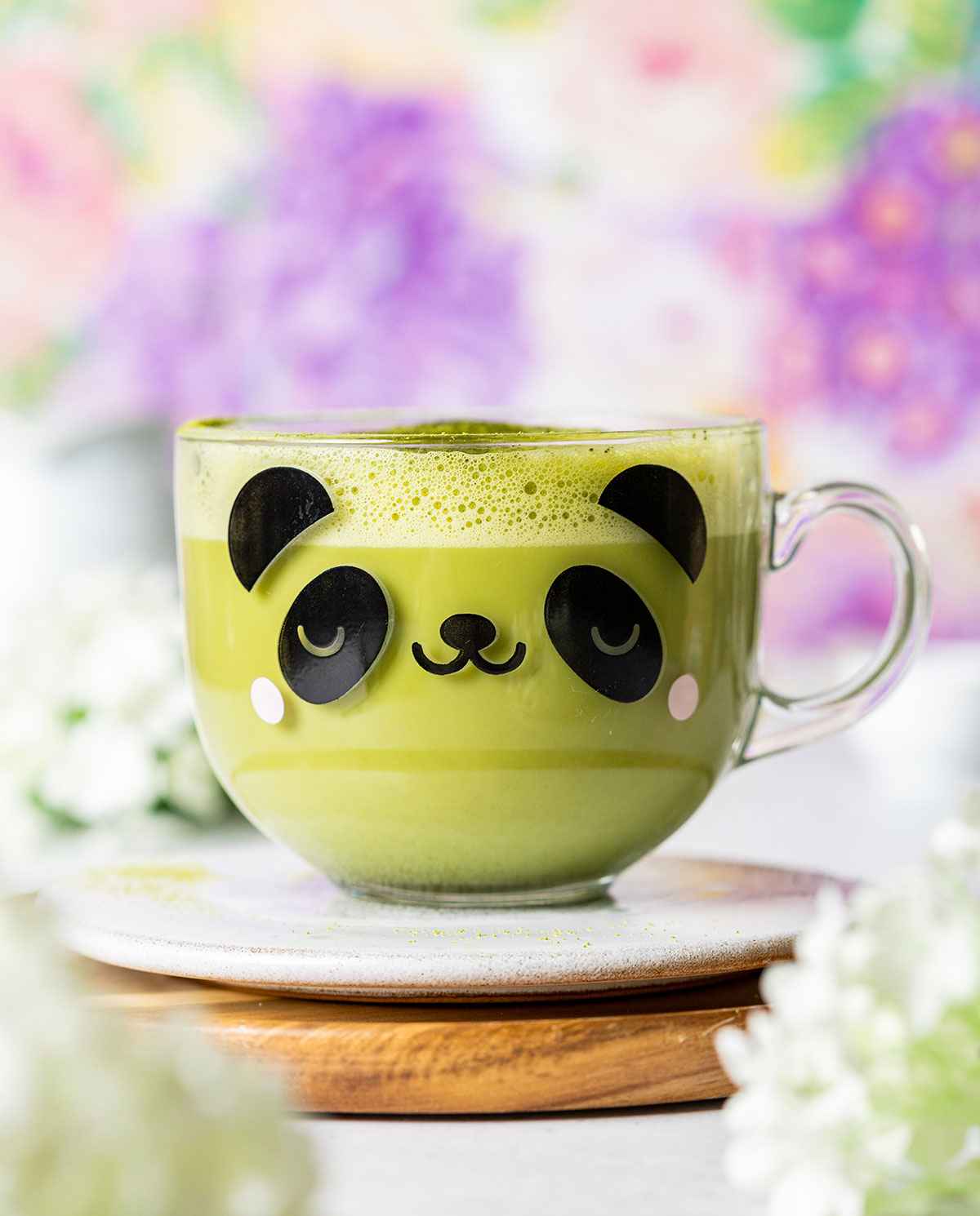a glass mug with a panda face on the front filled with starbucks matcha latte