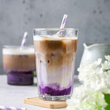 a glass filled with ube latte on a marble table