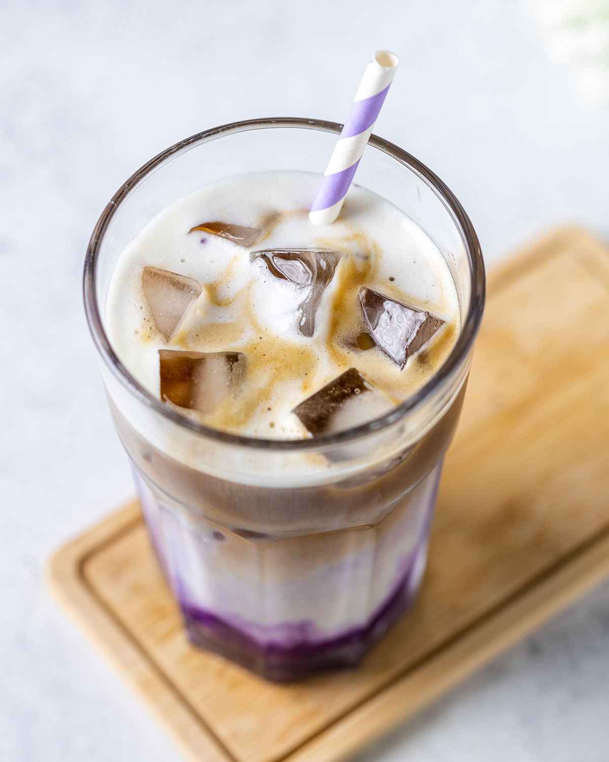 close up of the top of an ube latte in a tall glass with ice