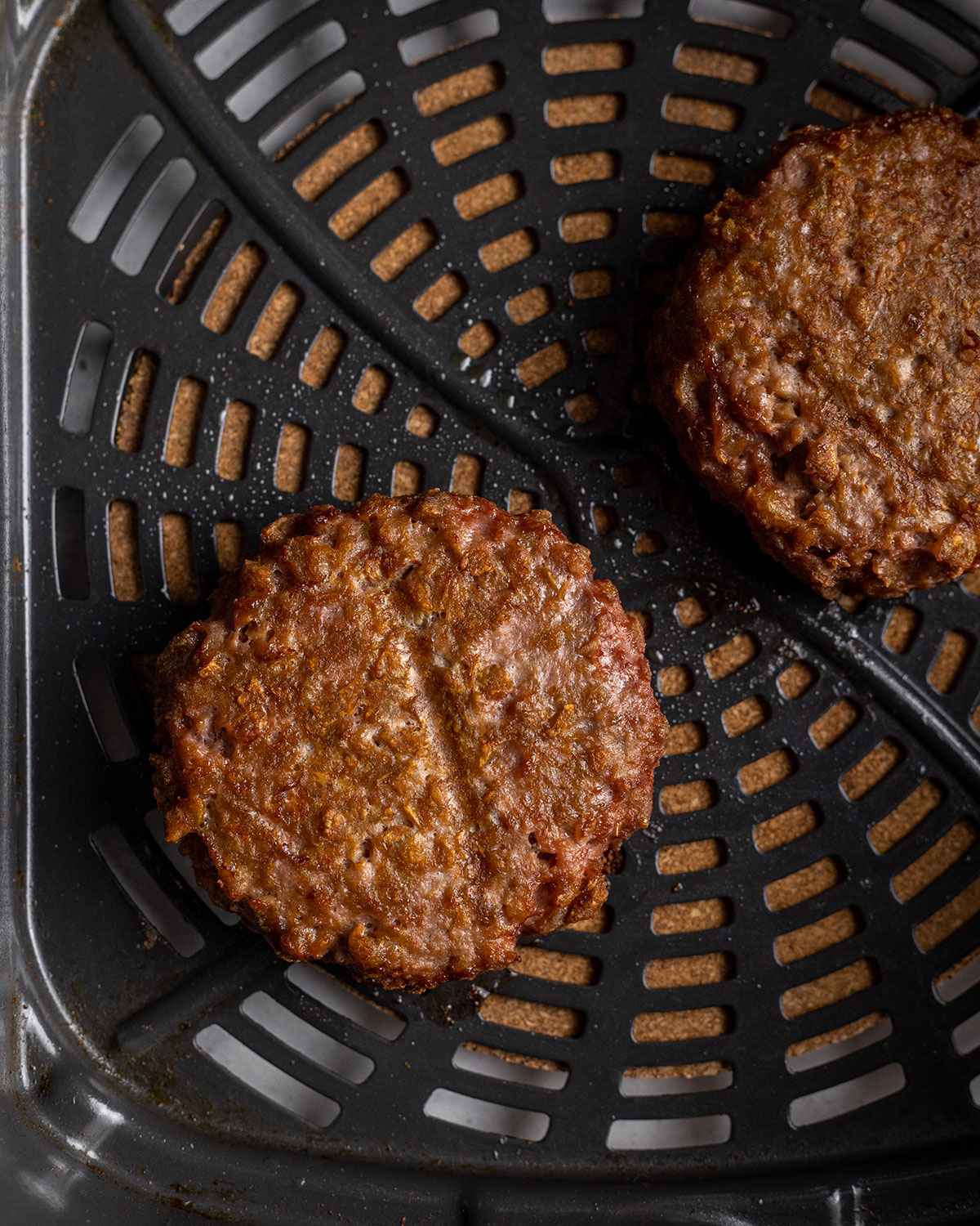 close up of two cooked burger patties in an air fryer